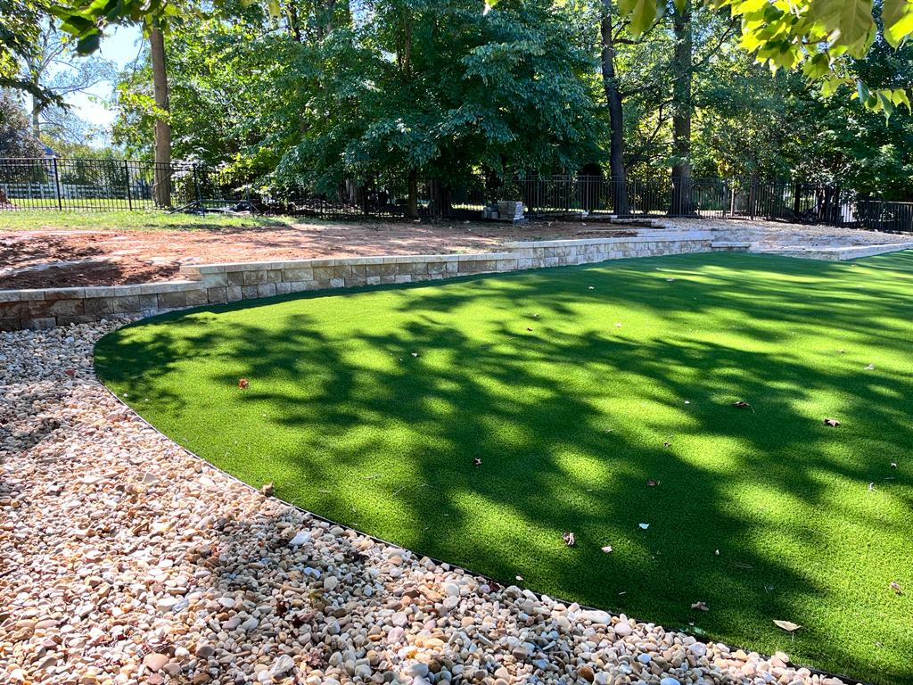 Artificial turf lawn with curved edging, river rock, and retaining wall in a McLean backyard.