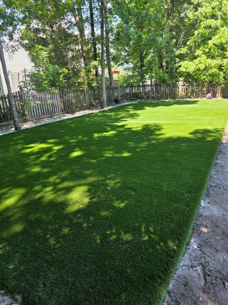 Large artificial turf lawn in a wooded residential backyard