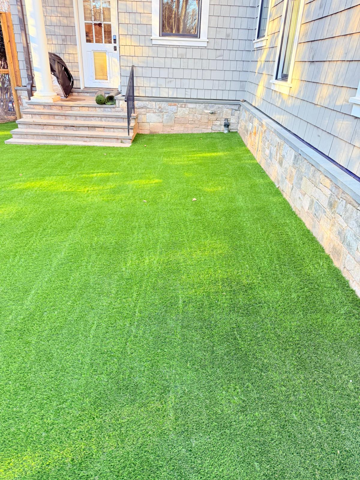 Artificial turf lawn installed beside a home with stone exterior and entry steps in McLean