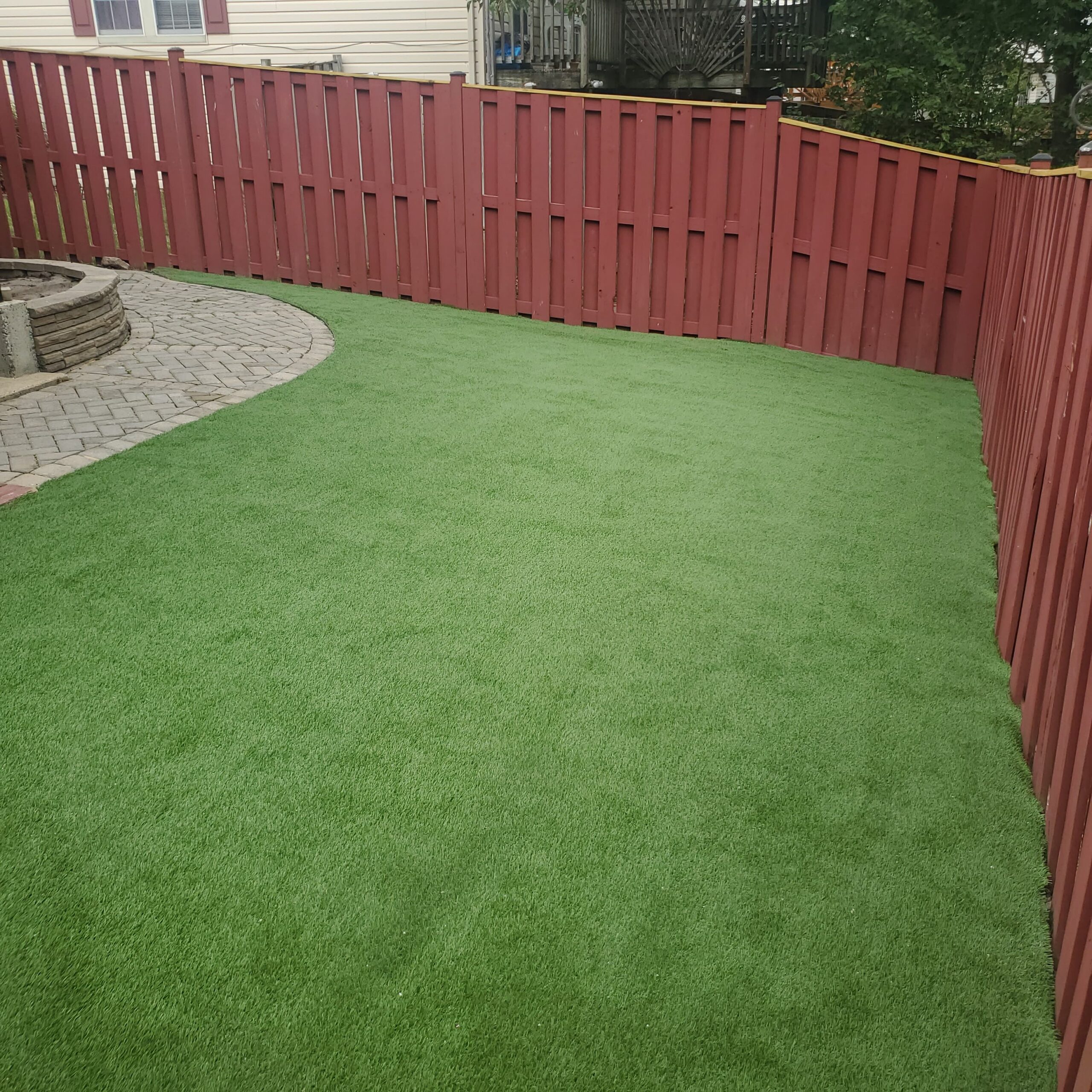 Artificial turf lawn surrounding a curved paver patio in a fenced Reston backyard