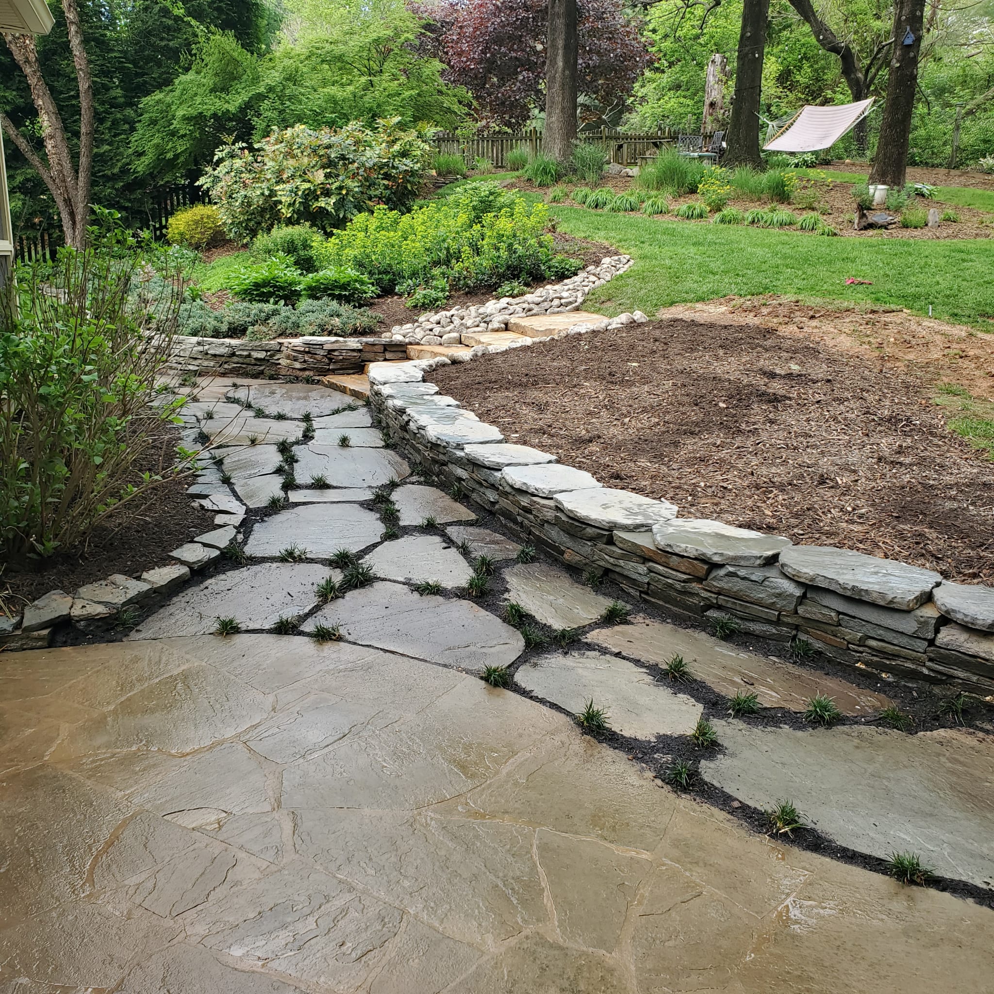 Natural stone walkway and stacked stone retaining wall surrounded by garden beds in a Vienna backyard