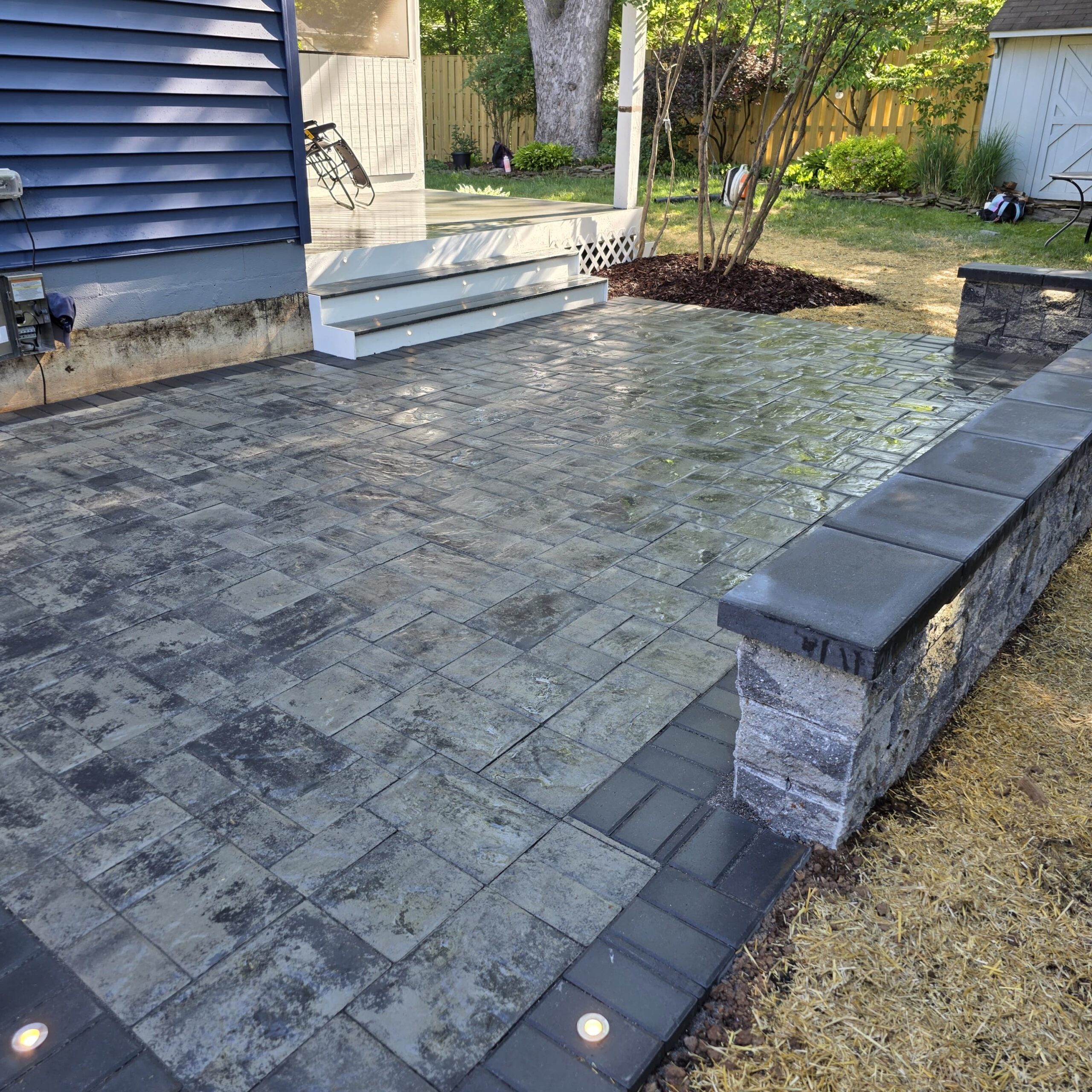 Paver patio with dark border, built-in lighting, and low seating wall in a Manassas backyard