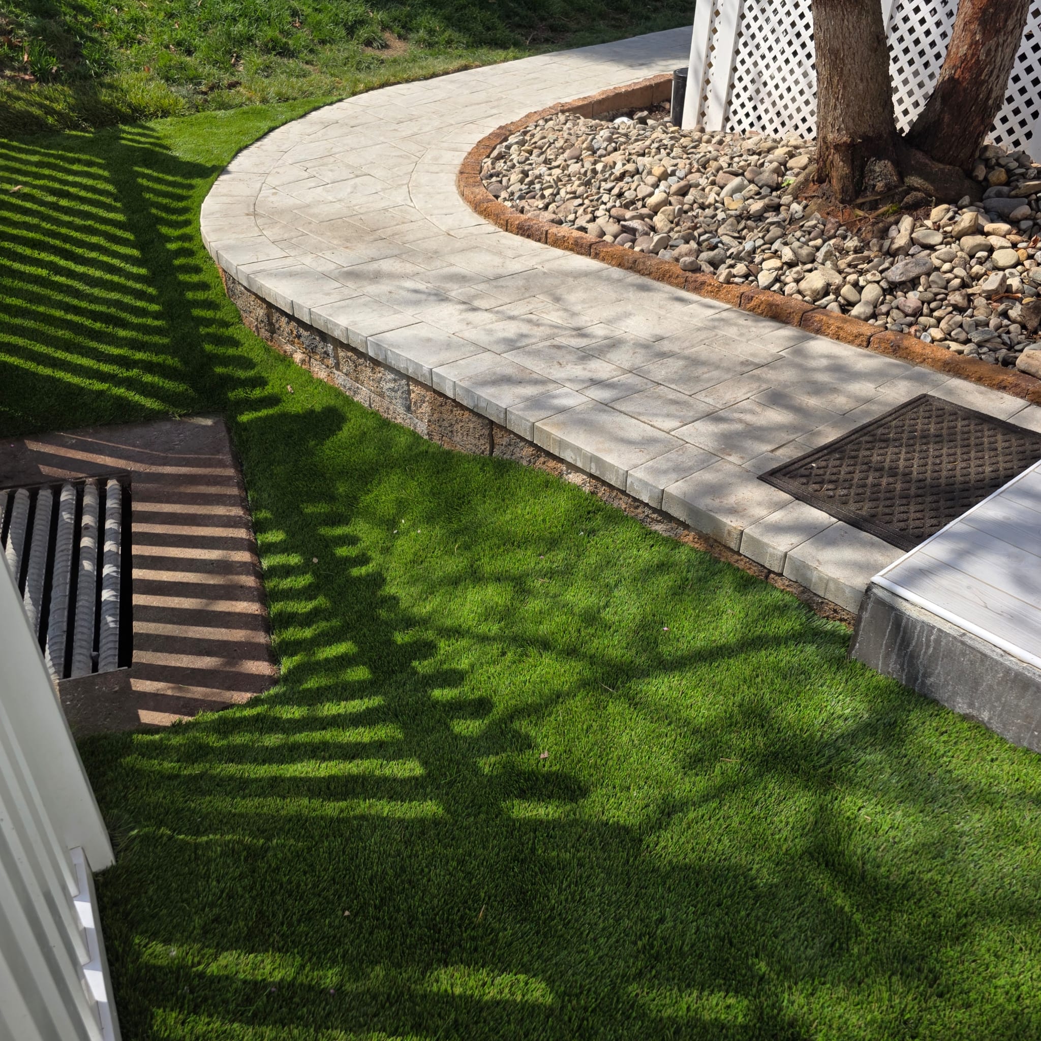 Curved paver walkway surrounded by artificial turf and decorative river rock in a Leesburg yard